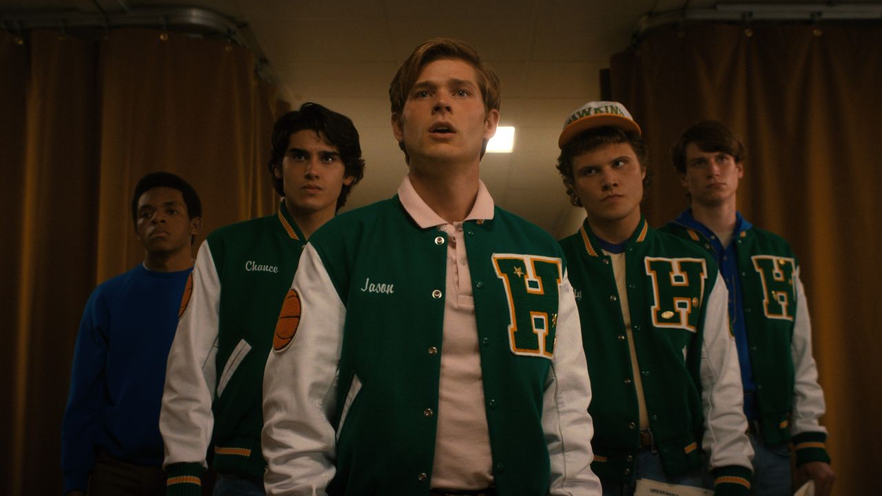 Group of guys standing in a row wearing letterman jackets in Stranger Things