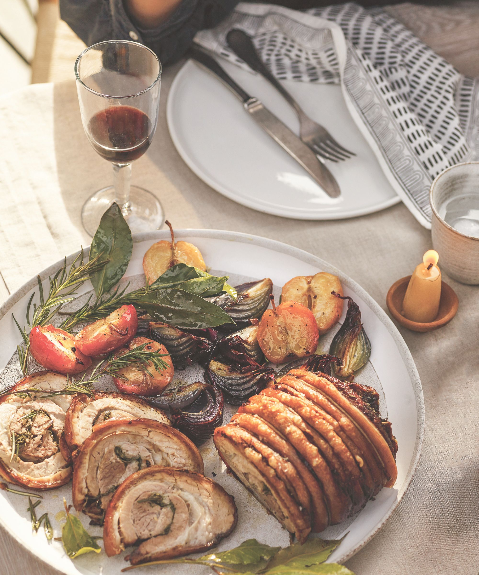 Rolled pork belly with apples and onions on a platter on a dinner table