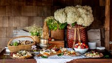 Rustic table set up with baskets and platters of food with baskets of flowers and a lace trimmed tablecloth