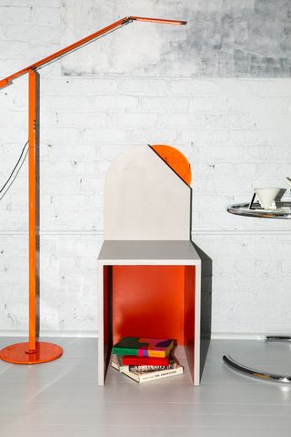 Standing orange lamp next to chair built into the wall next to a metal rounded coffee table.