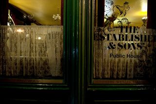 Upclose image of the pub entrance door with the text "The Established & Sons Public House" written on the glass section