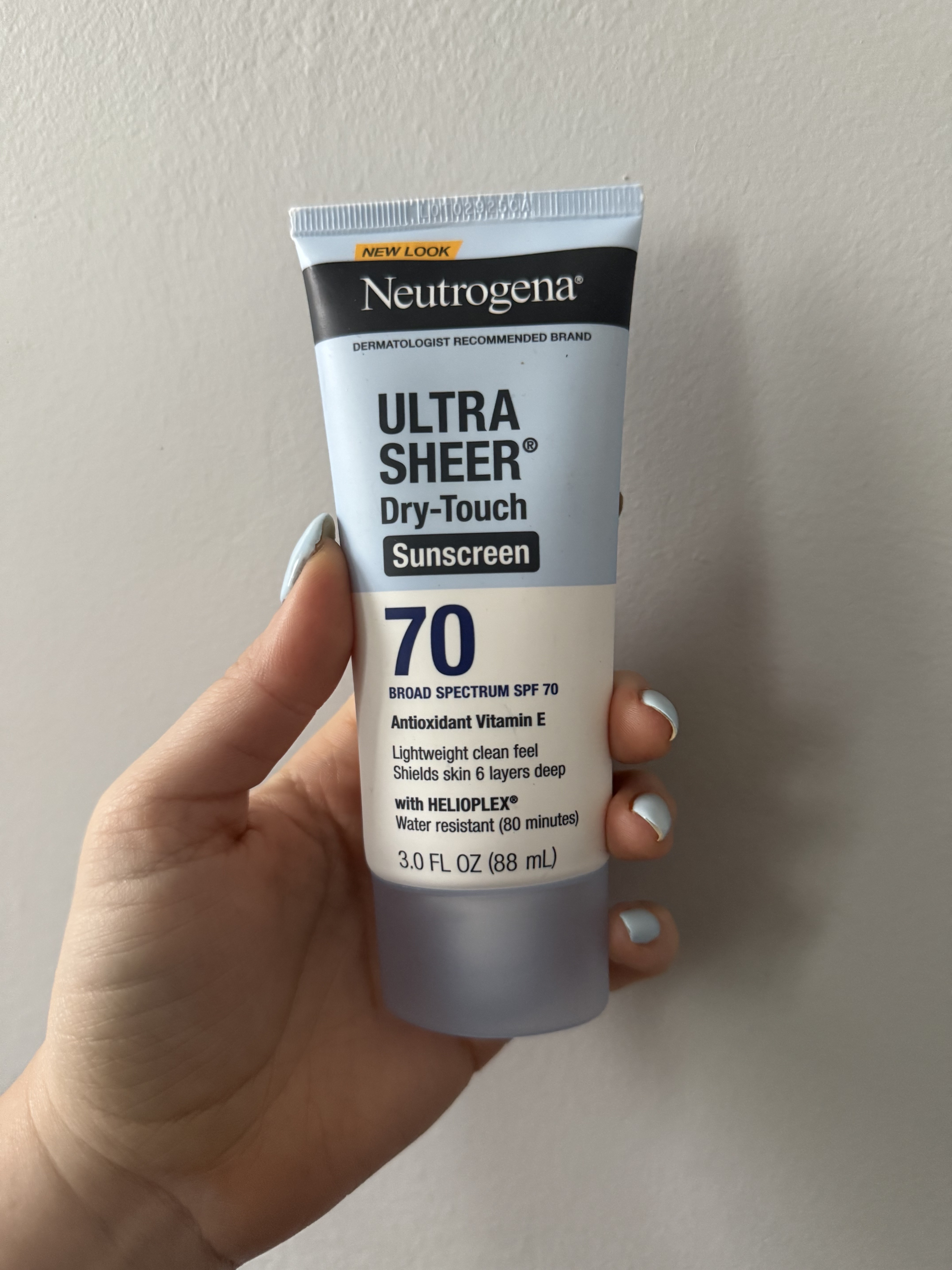 hand holding up Neutrogena Ultra Sheer Dry-Touch Water Resistant and Non-Greasy Sunscreen Lotion with Broad Spectrum SPF 70 on grey wall