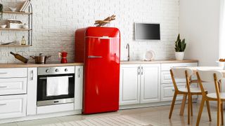 Red refrigerator with a bowl of utensils on top of it in a white kitchen