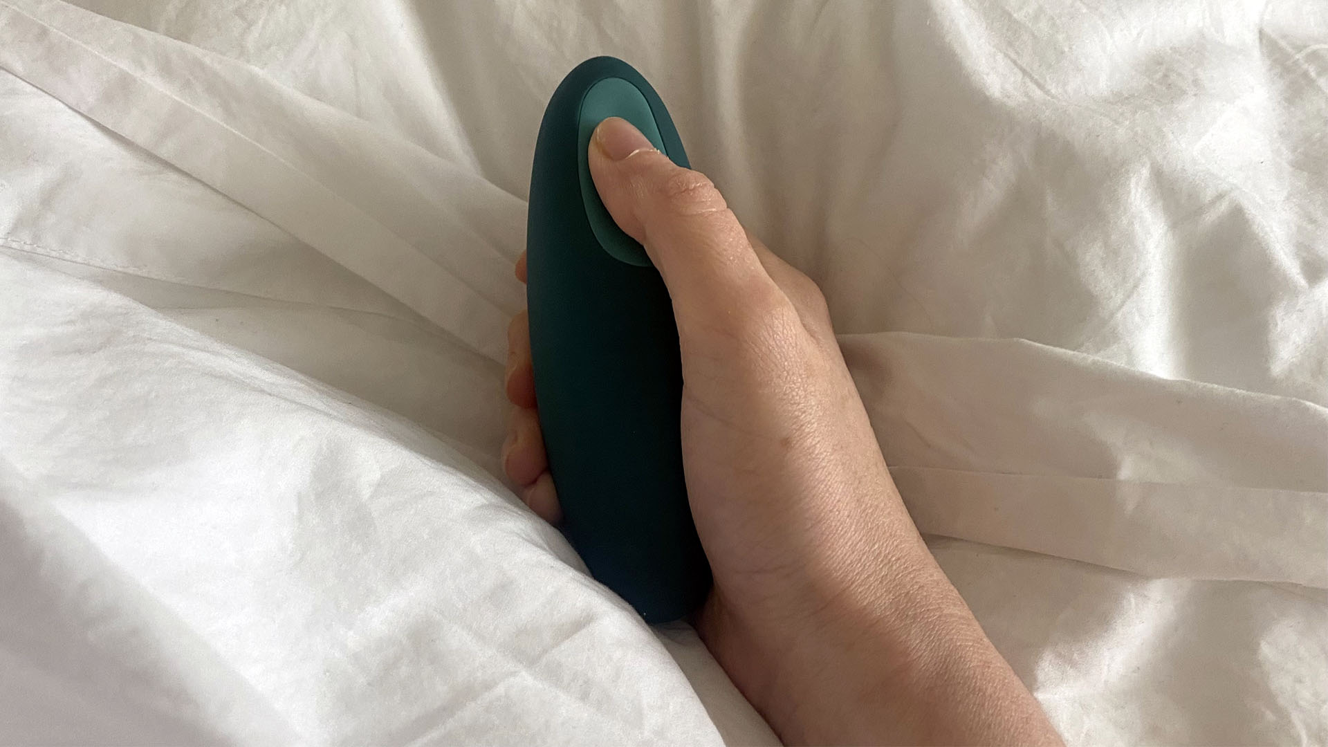 Our reviewer holds the moonbird handheld anti-anxiety device in bed, with her thumb on the sensor to activate the breathing mode