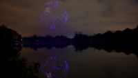A series of purple drones come together in the night sky above a still lake to create a 3D image of planet Earth with the continent of Africa seen and reflected in the lake