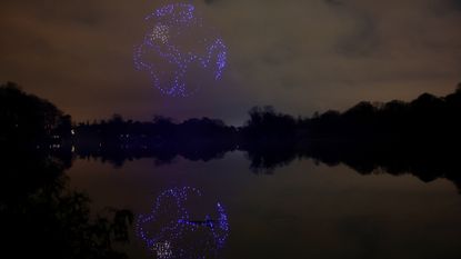 A series of purple drones come together in the night sky above a still lake to create a 3D image of planet Earth with the continent of Africa seen and reflected in the lake