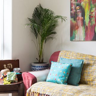 living room with white wall painting on wall plant and sofa with designed cushion