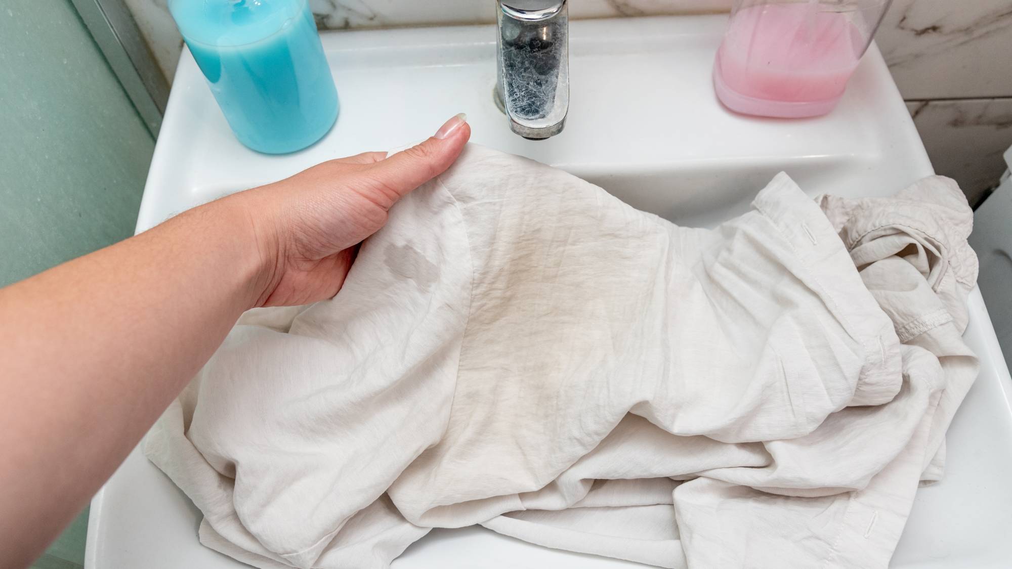 Person holding a yellowed white shirt over a bathroom sink before soaking it to restore dingy laundry.