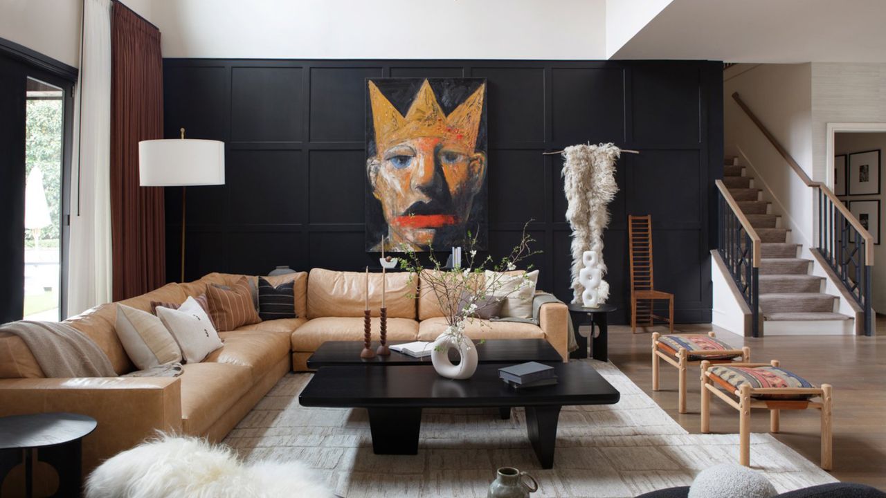 Living room with black panelling against white wall, tan sofa and black coffee table