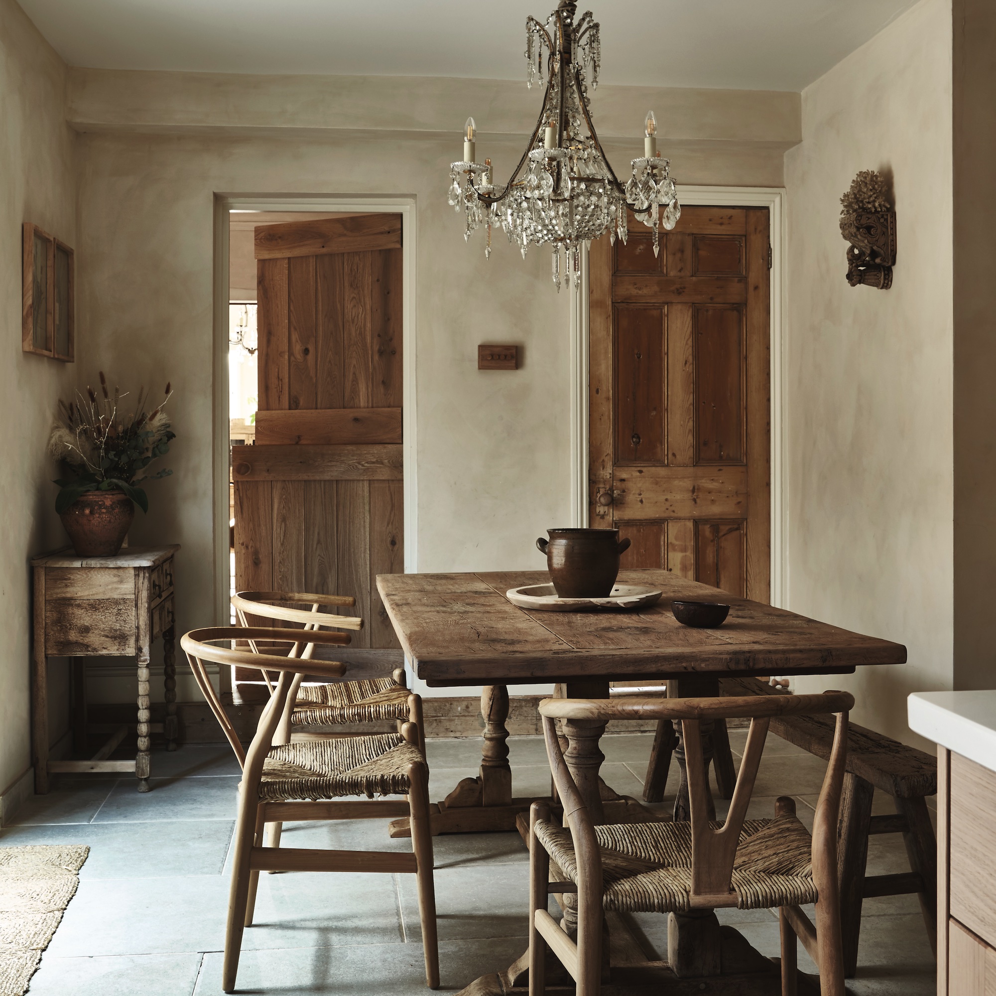 dining area in kitchen with limewash walls, with farmhouse table and wishbone chairs with rush seating, and antique crystal chandelier