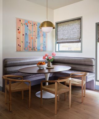 dining nook with purple seating corner bench, three wooden chairs, round table and white walls with artwork and window with blind