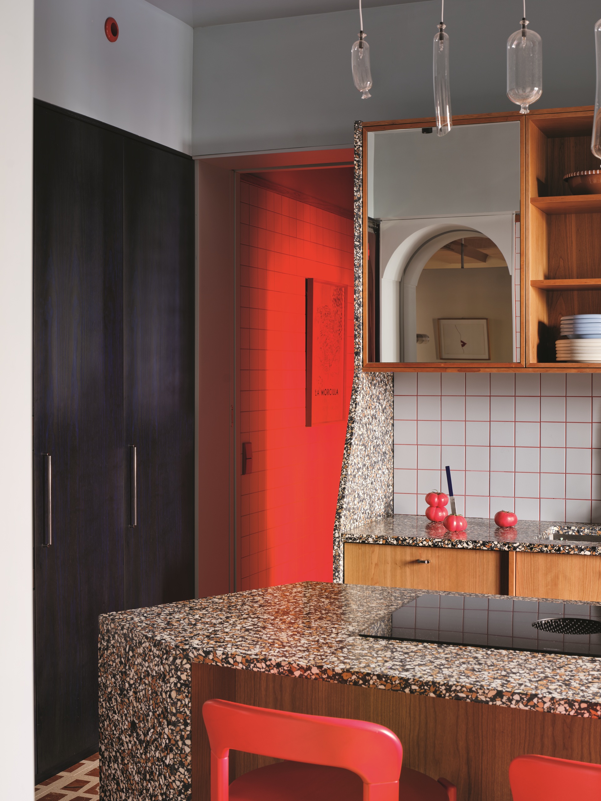 angled terrazzo kitchen island with red chairs, black cabinets, square tiles with pink grout, and timber joinery