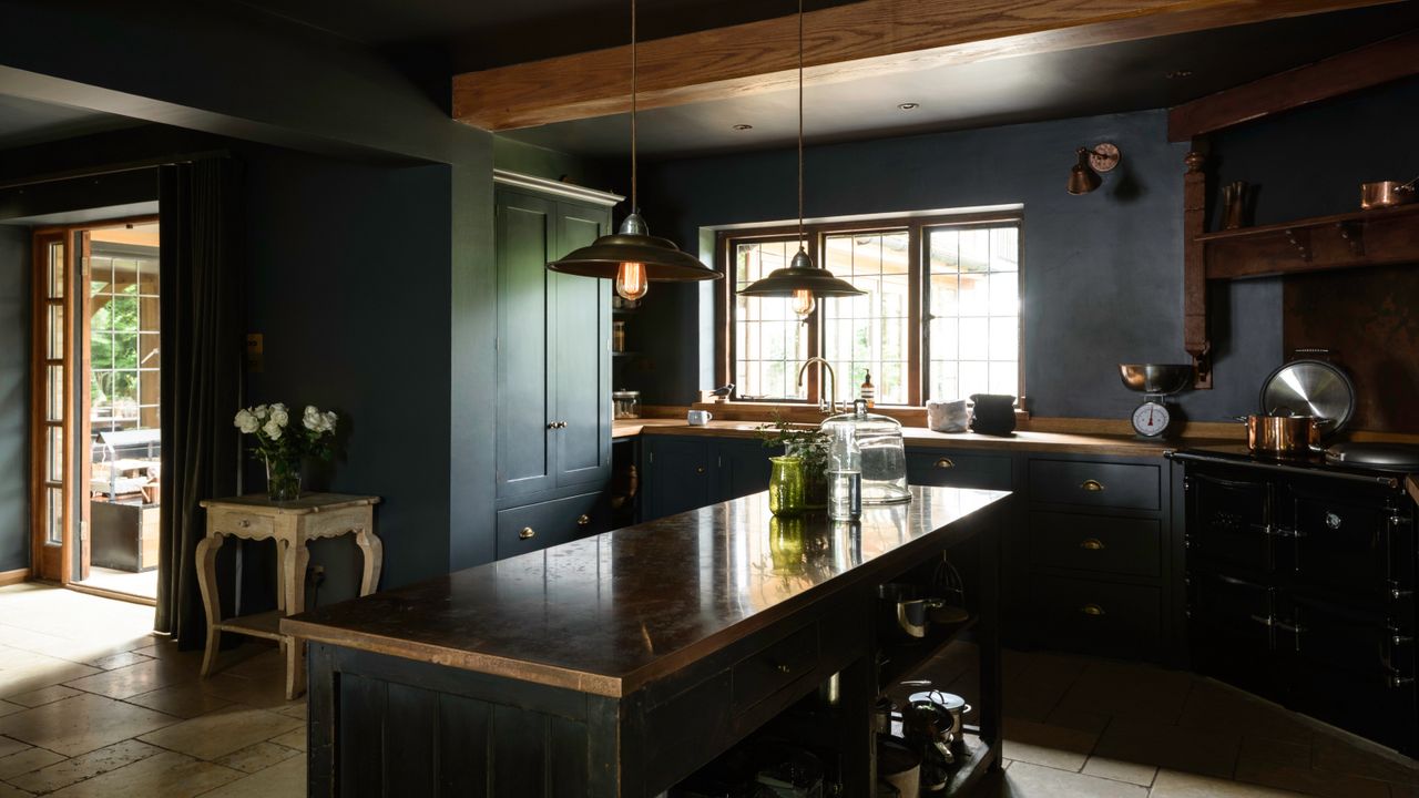 dark blue kitchen with beams, color drenched, small kitchen island, wooden and copper countertops, glassware, pendant lights, black oven, deVOL