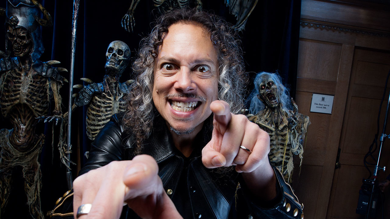 A photograph of Kirk Hammett in front of some creepy skeletons