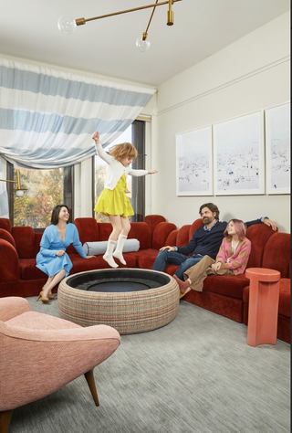 A living room with a bright red couch, a gray carpet, a coffee table with storage inside, and a striped blue curtain