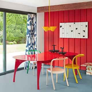 Dining room with red panelled wall, red table, and yellow chairs