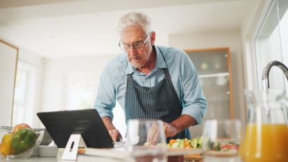 Senior man cooking and looking at recipe on his tablet