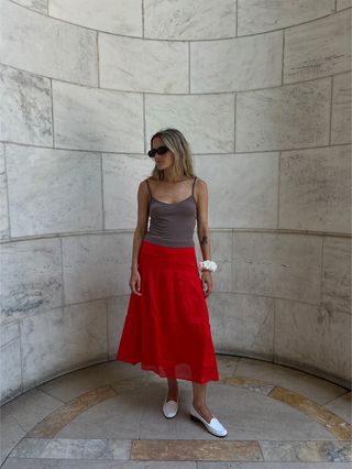 Eliza Huber wearing a red midi skirt, tan camisole, white loafers, and white scrunchie from the J.Crew x Maryam Nassir Zadeh collaboration.