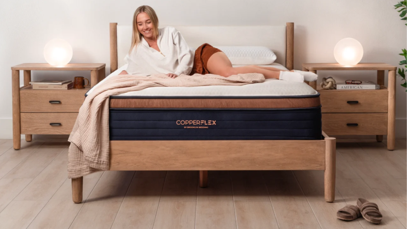 Blonde woman laying on Brooklyn Bedding CopperFlex mattress in bedroom with wooden floor, wooden bed base and two bedside tables 