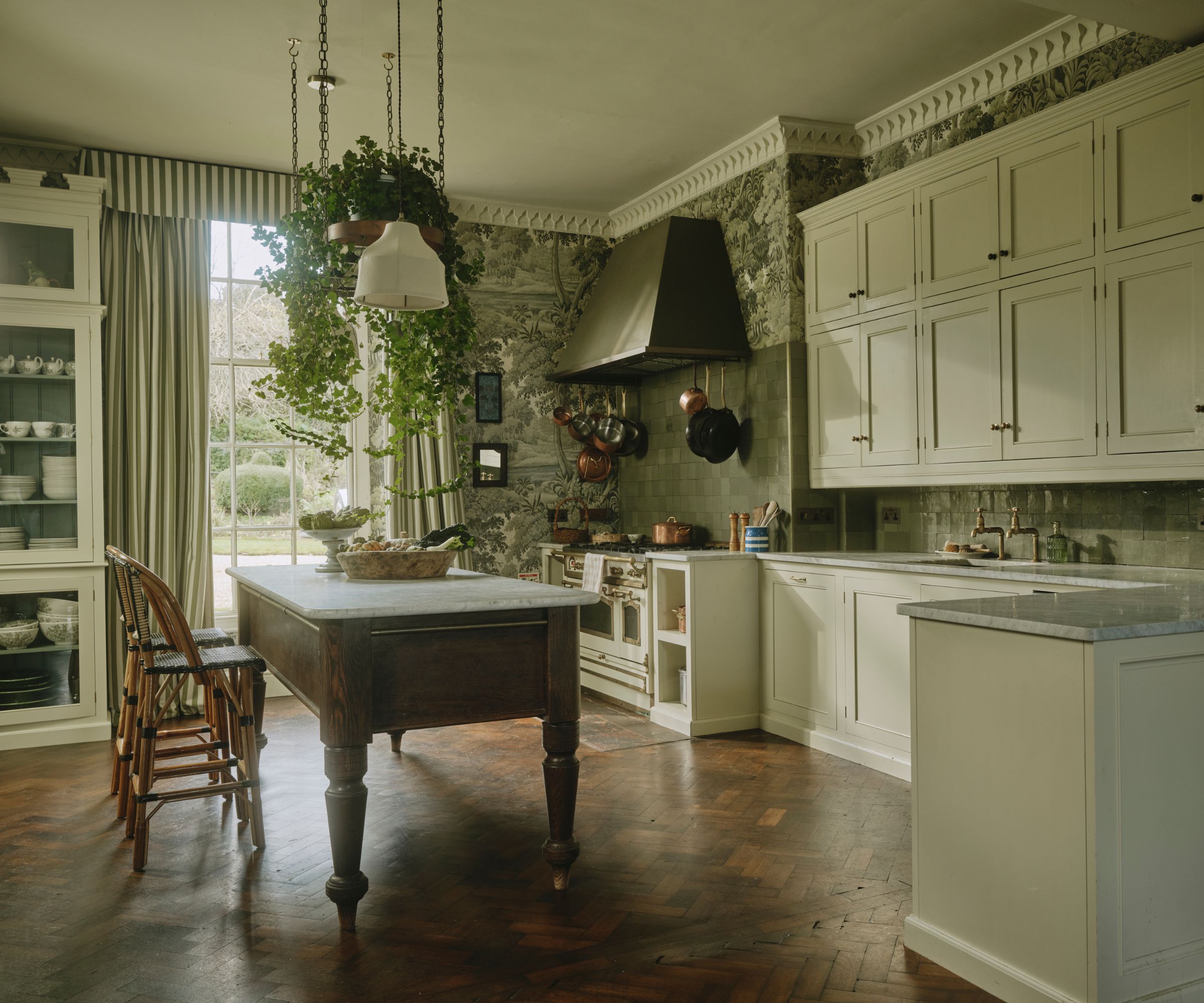 A large kitchen with white cabinets, marble countertops, botanical wallpaper on the walls and castellations on the top of the cabinetry