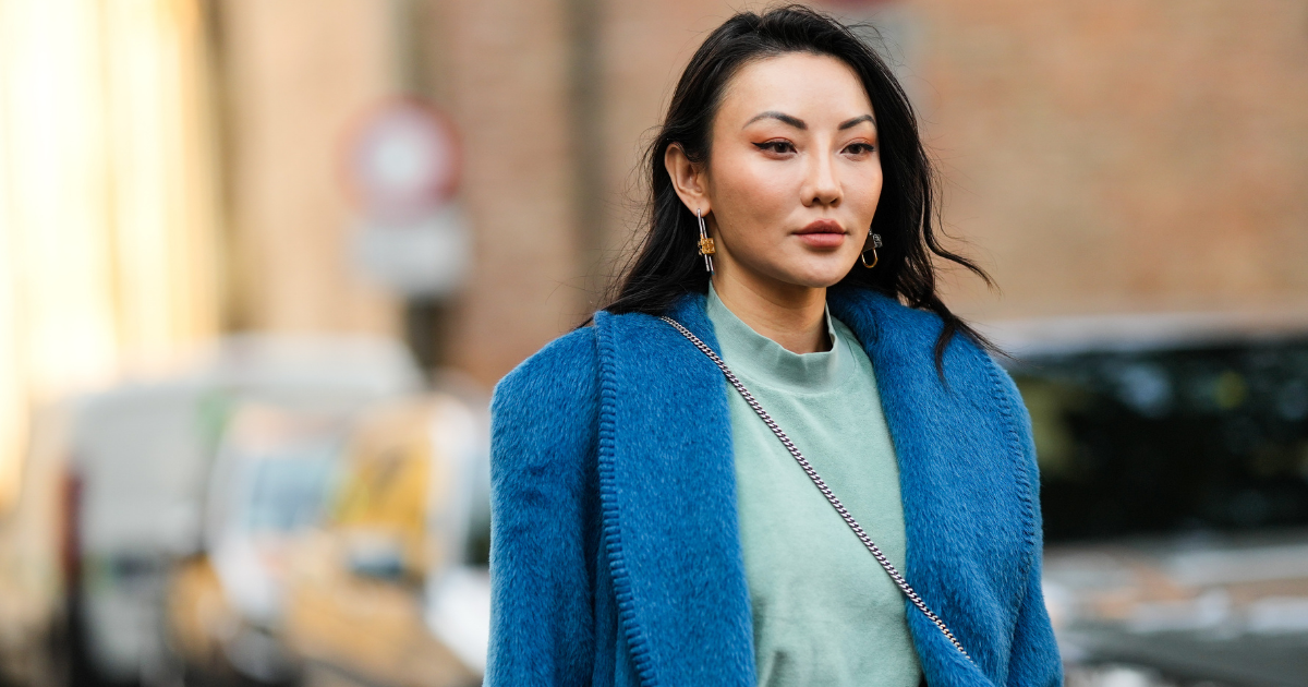 End of filler Jessica Wang wears a silver and gold pendant earrings, a pale green t-shirt, a dark green midi skirt, a blue fluffy oversized long coat,
