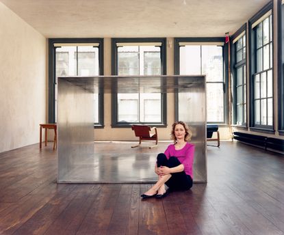 Donald Judd’s daughter Rainer sits on the wooden floor, posing in front of the hollow metal cube.
