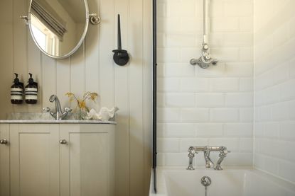 A modern bathroom with cream wood panelled wall, a built-in vanity, and subway tiled bath 
