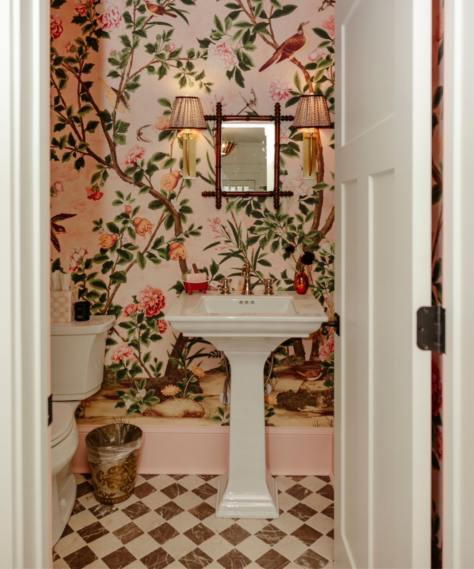 A powder room decorated with pink bird-themed wallpaper, a white pedestal sink, and vintage accessories