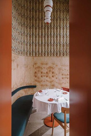 Interior of the Opasly Tom restaurant in Warsaw with patterned walls, blue seating and a table with white tablecloth