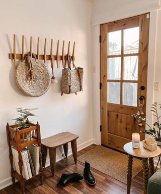 An entryway with a brown door, a wall hanger with vertical hooks, a wooden table, and black boots on the floor