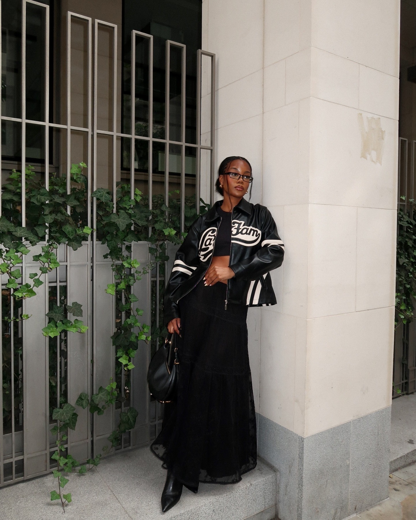 Fashion Person Tobi Ojora wears a black leather jacket black and white cropped t-shirt, black full lenght lace skirt and black pointed toe heeled boots in a recent image from her Instagram.