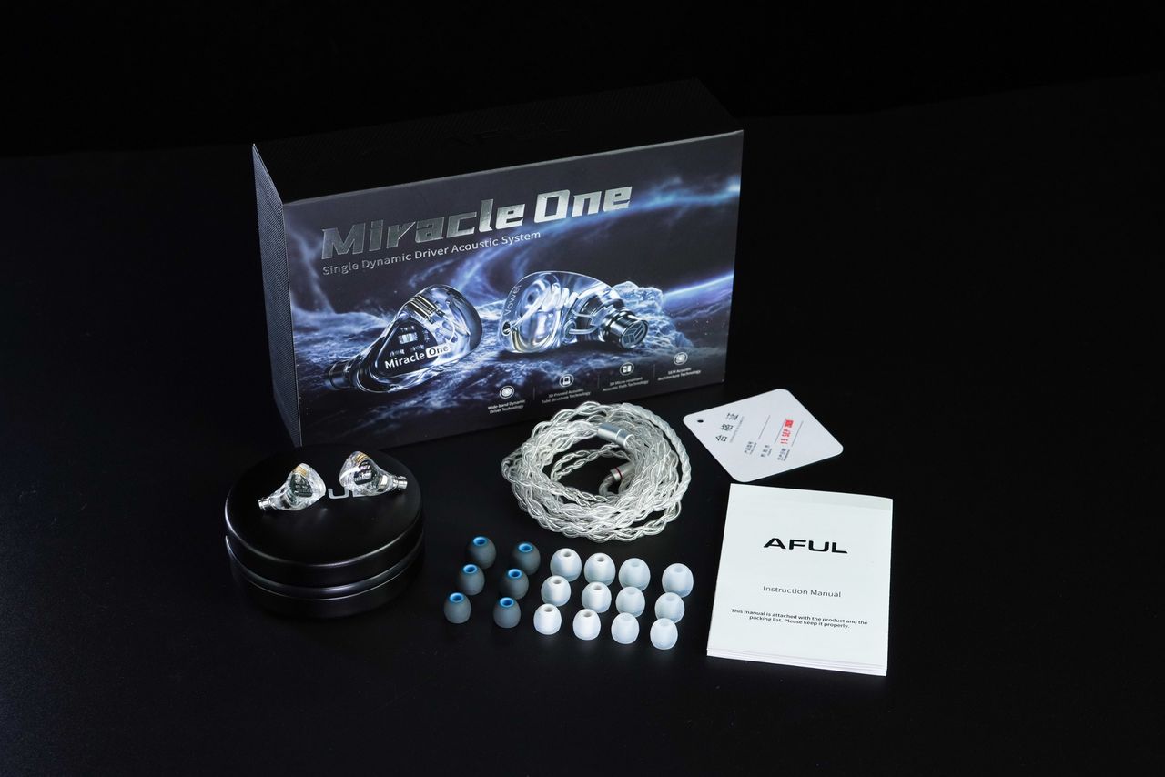 The Aful MiracleOne box contents on a black surface: the retail box, the clear earbuds on a round black case, a coiled silver cable, nine pairs of grey and white ear tips and the instruction manual