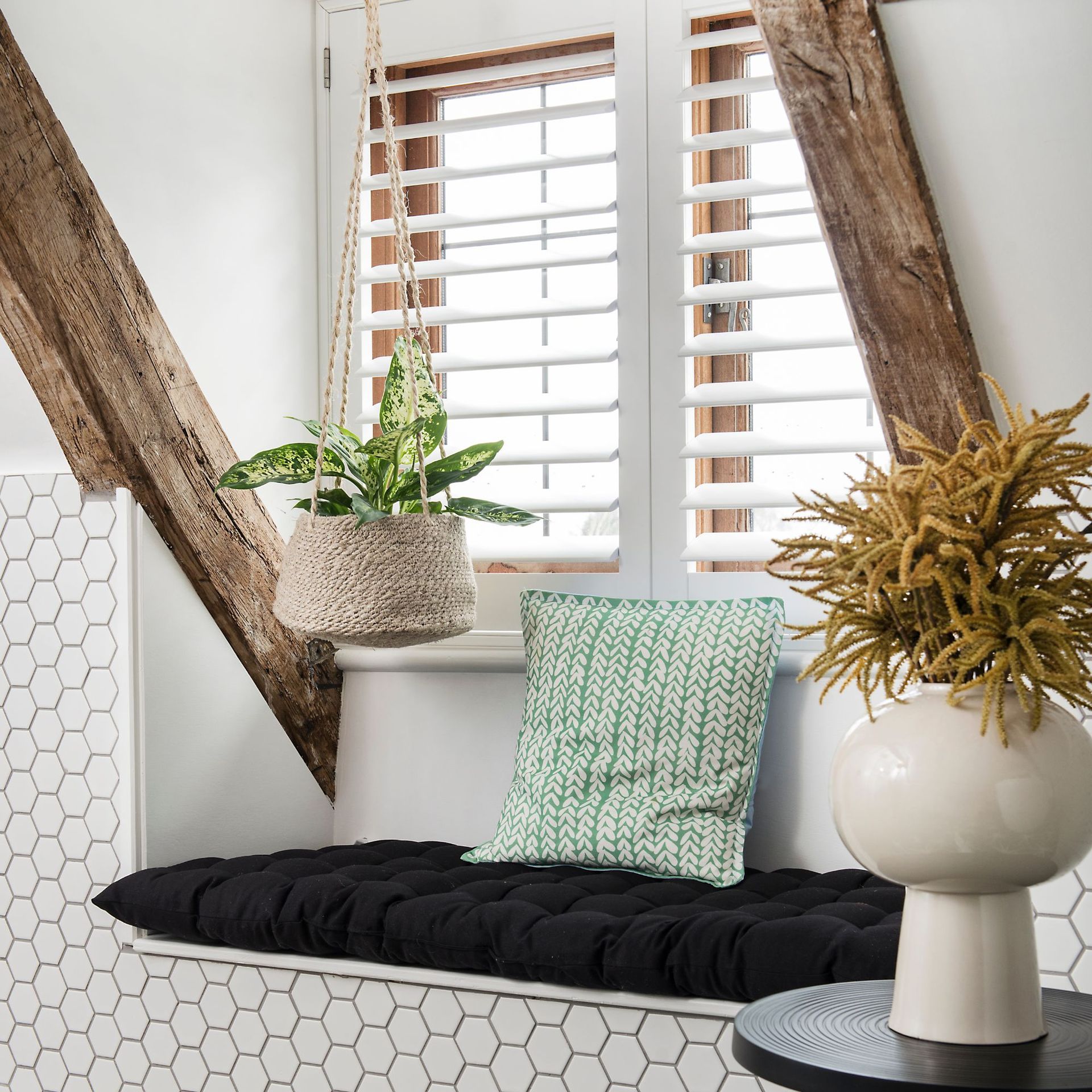 A small seat below a shuttered window with handing houseplants