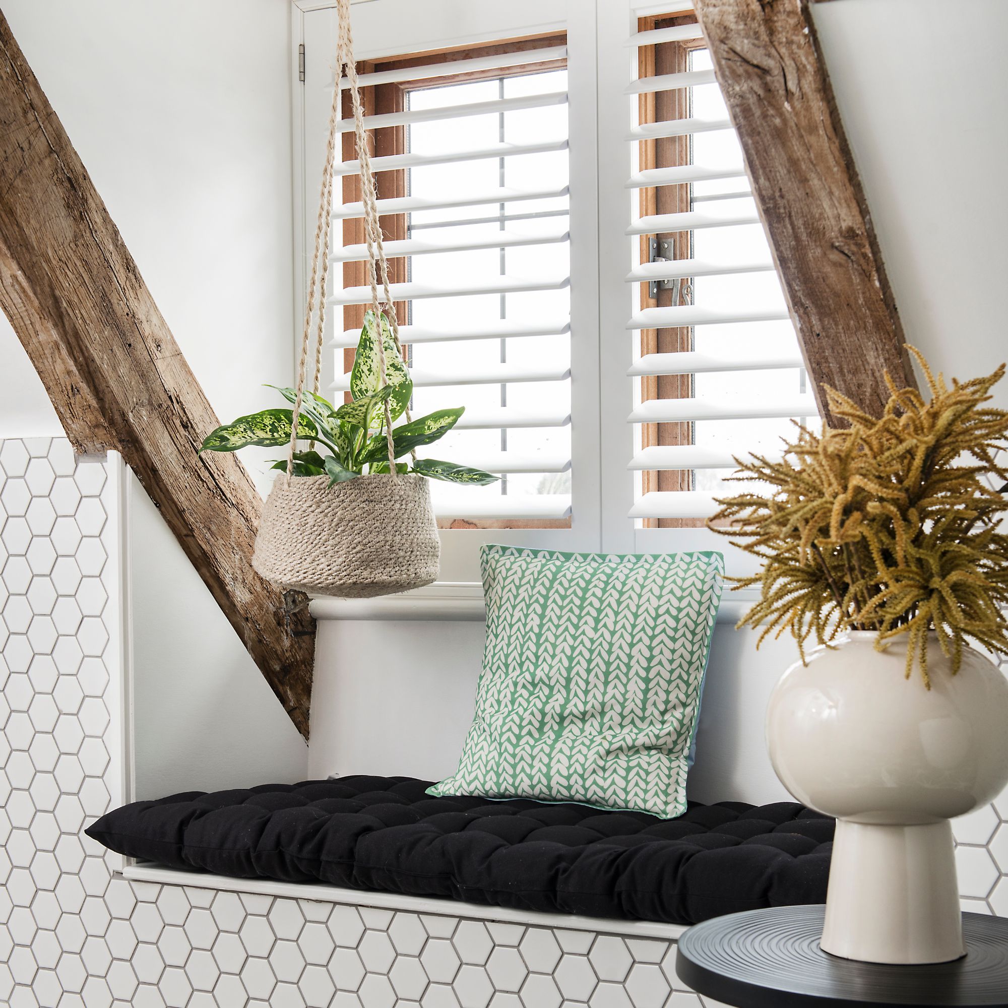A small seat below a shuttered window with handing houseplants