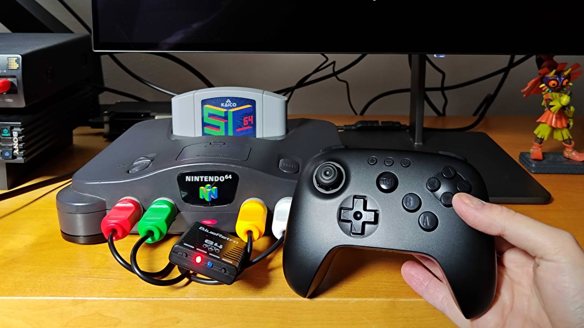 Close up of hand holding 8Bitdo N64 Bluetooth controller next to console with Blueretro wireless adapter connected.