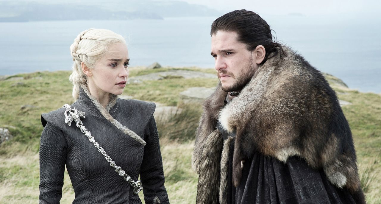 emilia clarke as dany and kit harrington as jon snow standing on a cliff by the sea in game of thrones