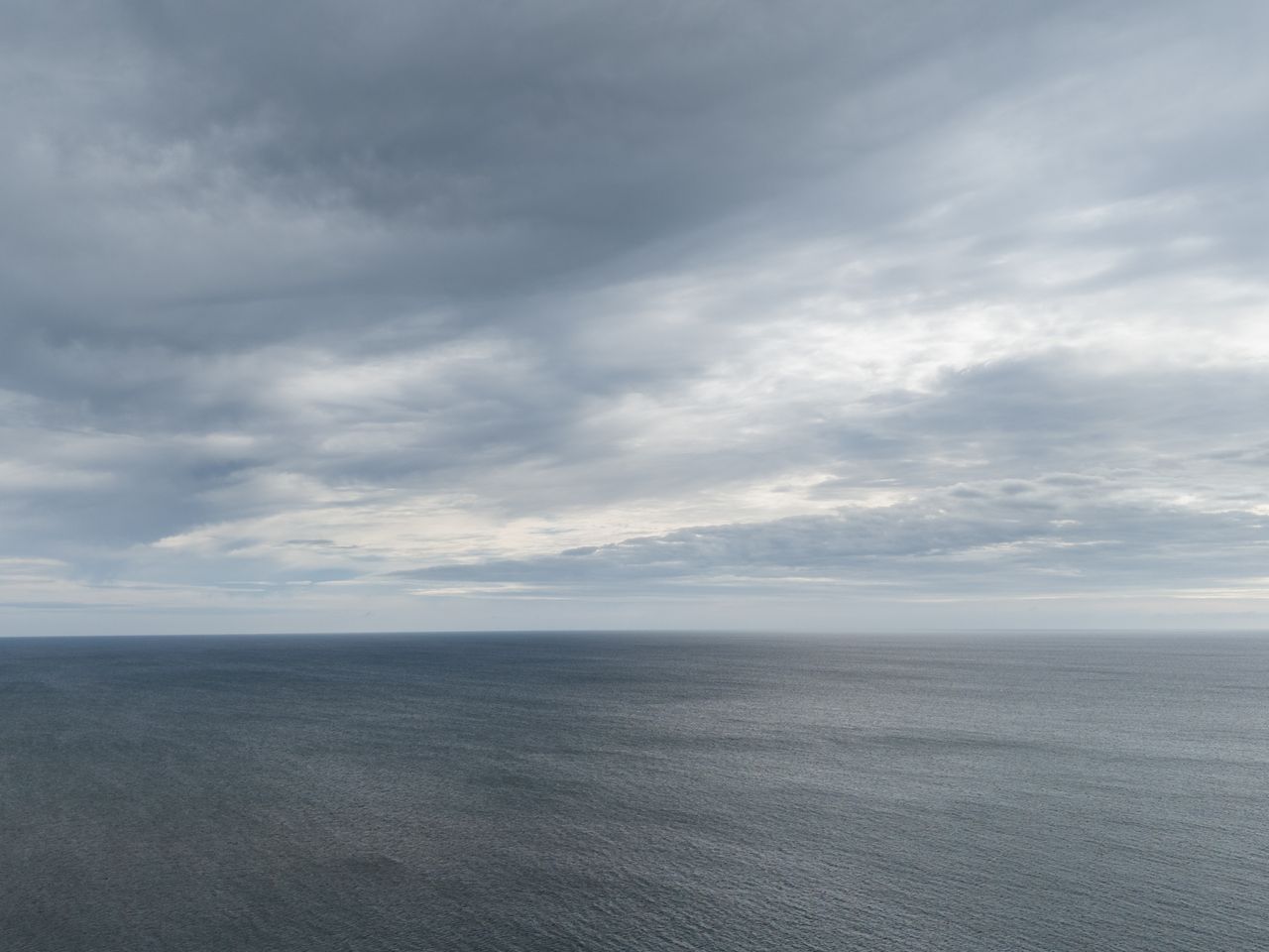 Image taken by DJI Air 3 (a camera drone). Here we see the gray sea meeting the gray cloudy sky.