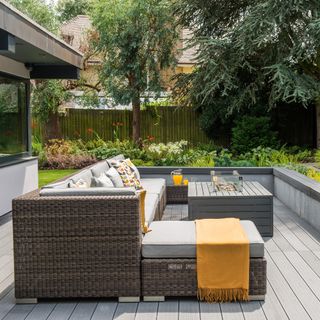 a decked area of a garden with a large corner outdoor sofa with cushions and a firepit table