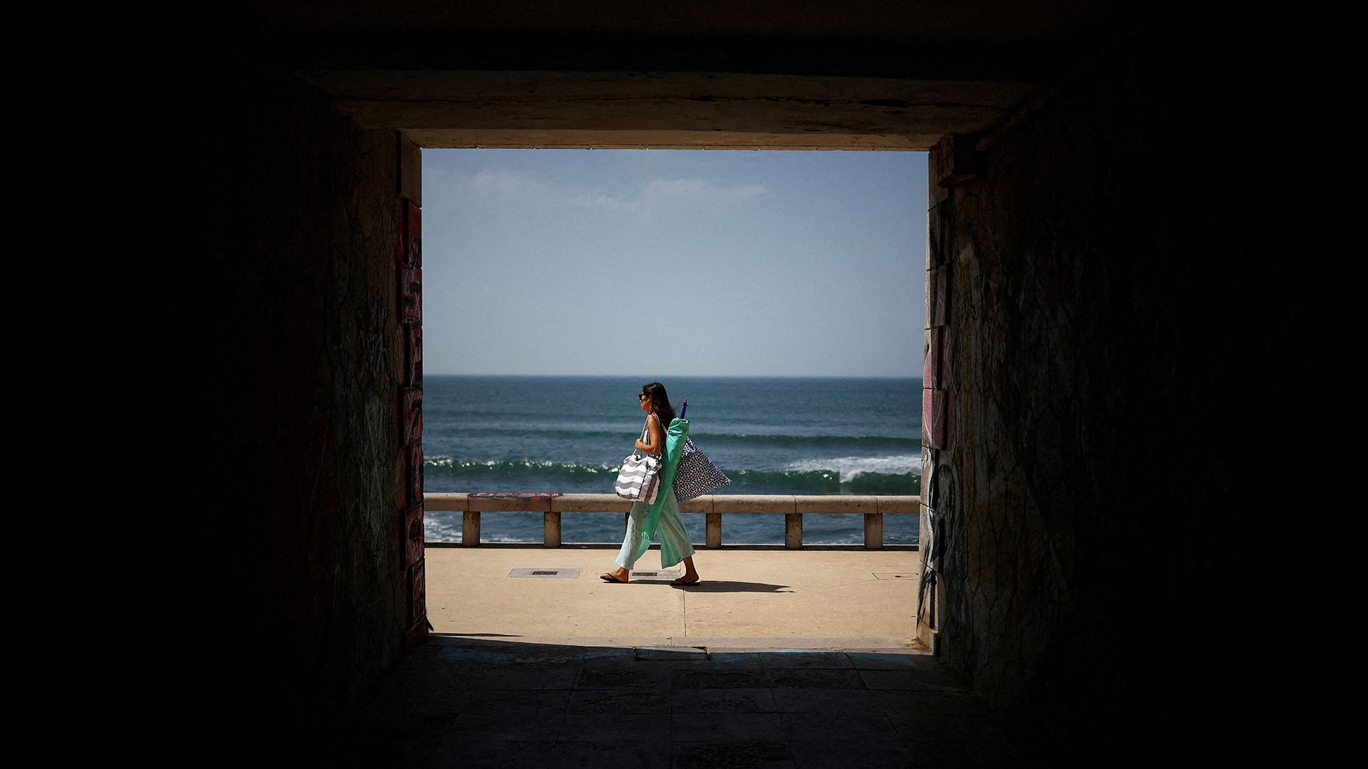 
                                A woman arrives at Parede Beach during a heatwave in Cascais, Portugal
                            