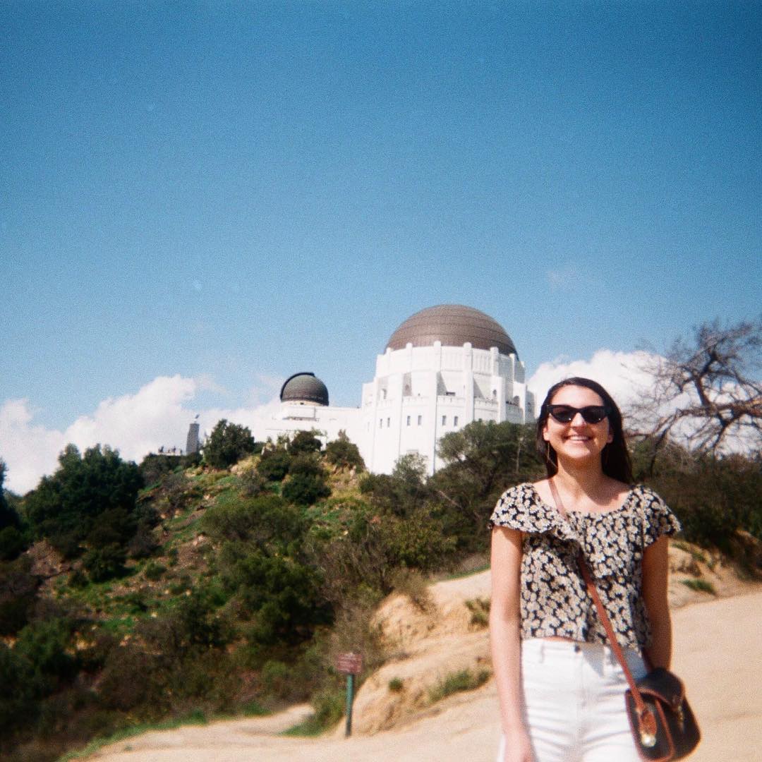 Woman standing in front of Griffith Observatory wearing a floral shirt, crossbody bag, and ecru jeans.