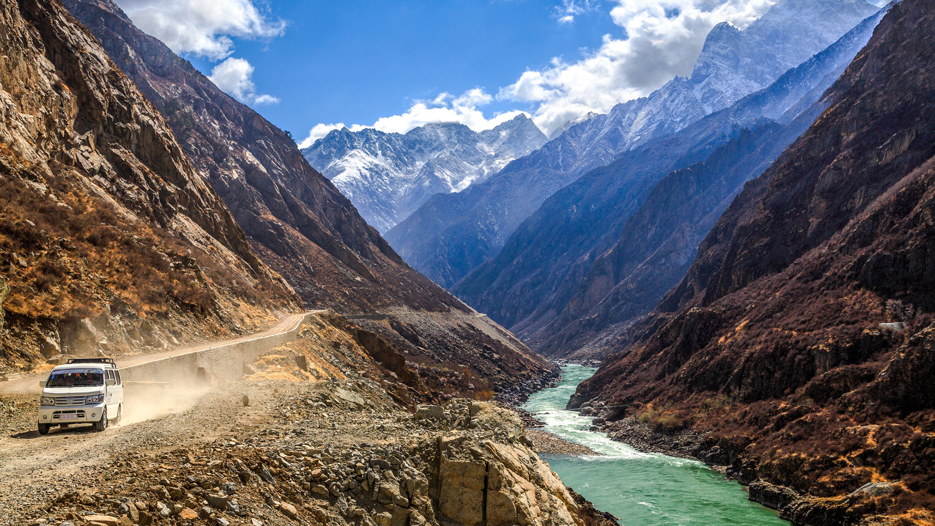 A car drives on a dirt road in a valley next to a river.