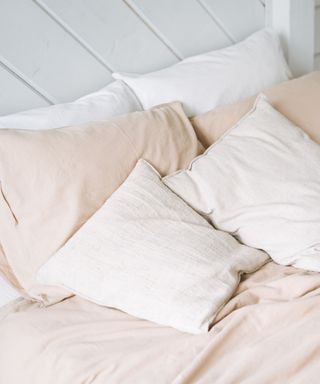 A bed with a beige duvet, white pillows, and a white wooden bed frame