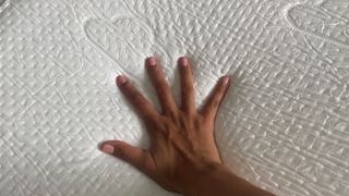 A hand pressing down on the Puffy Deluxe Mattress Topper
