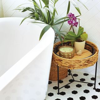 White freestanding bath with woven side table and black and white tiled floor