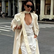 @thecarolinelin carries an ecru handbag under her arm whilst wearing a cream coat, white top and white trousers