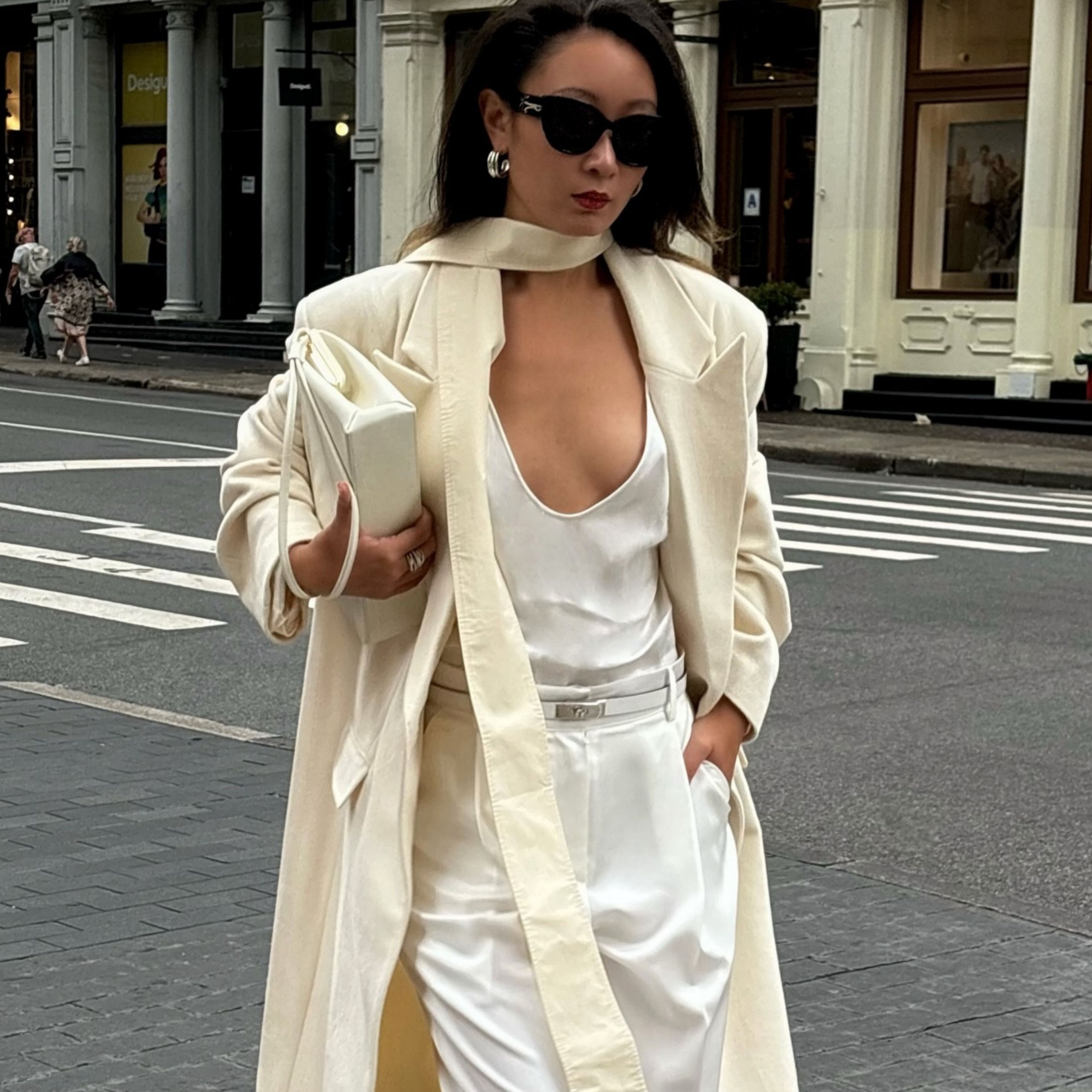 @thecarolinelin carries an ecru handbag under her arm whilst wearing a cream coat, white top and white trousers