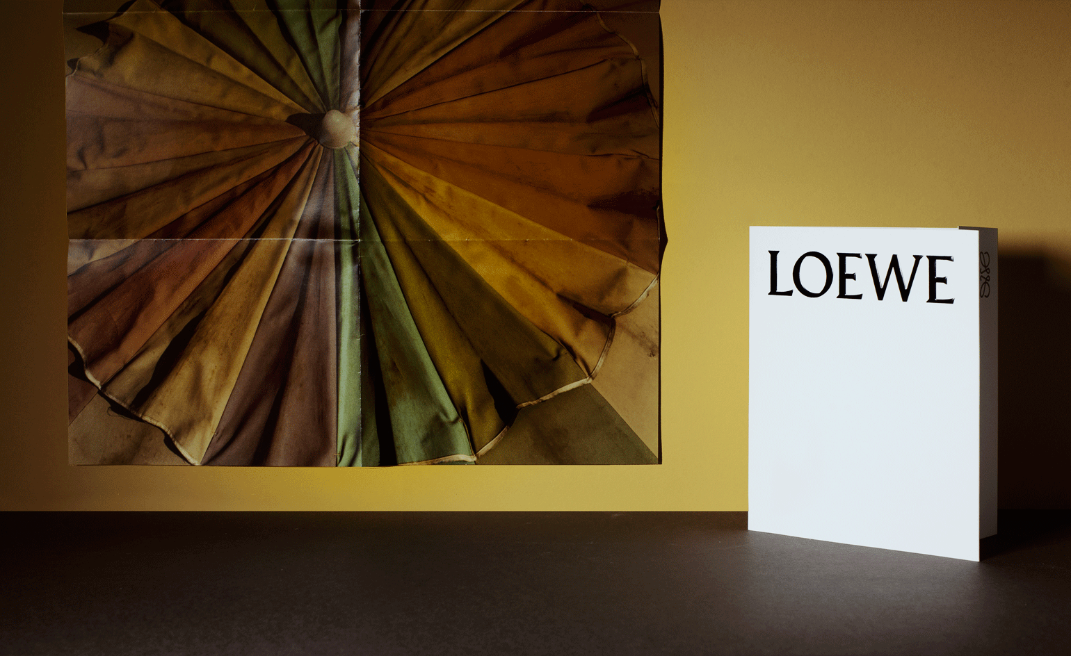 A large debossed logo on a crisp white gate-folded card accompanied a poster of an aged beach umbrella from Loewe