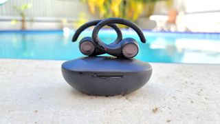 The Tribit MoveBuds H1 wireless earbuds and charging case displayed by a pool