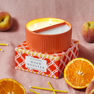 An orange candle surrounded by oranges and apples.