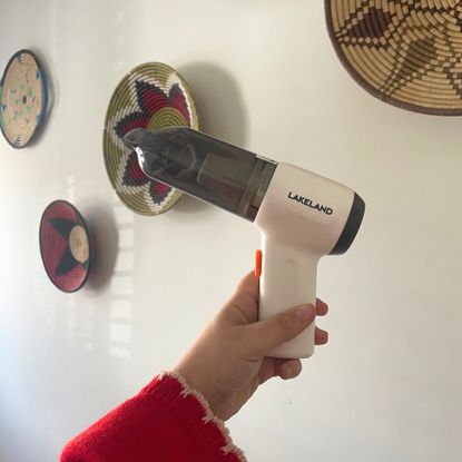 Hand holding the Lakeland 3-in-1 Mini Vacuum Cleaner up against a white painted wall